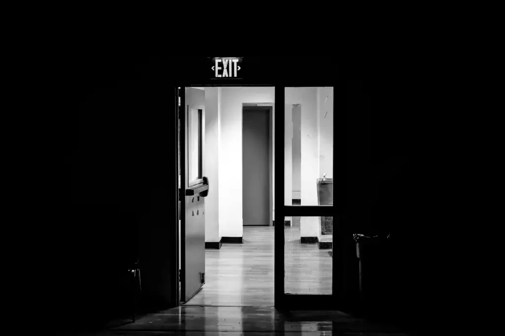a dark room where there is a door with an EXIT table which is leading to the next light room