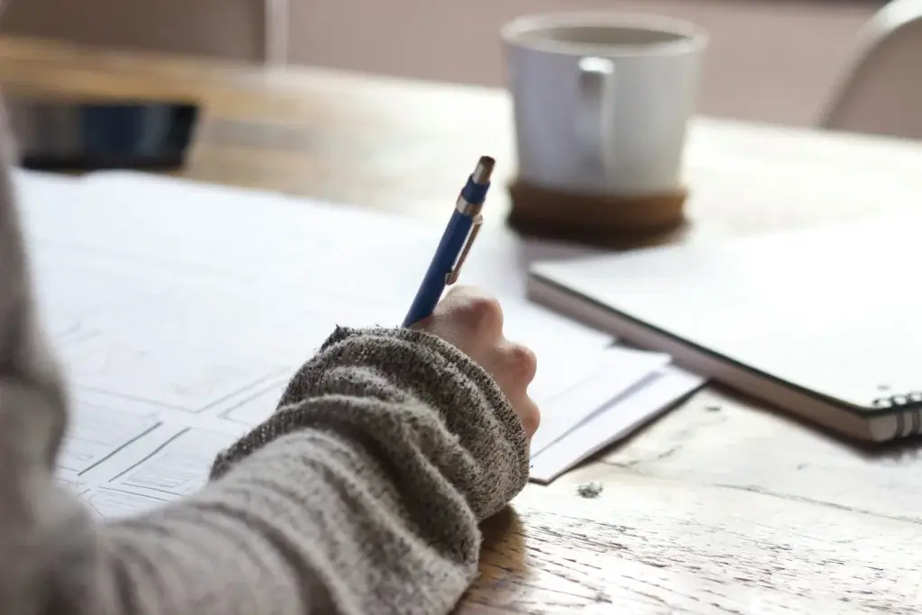 a person with a cup is writing on the paper his plans