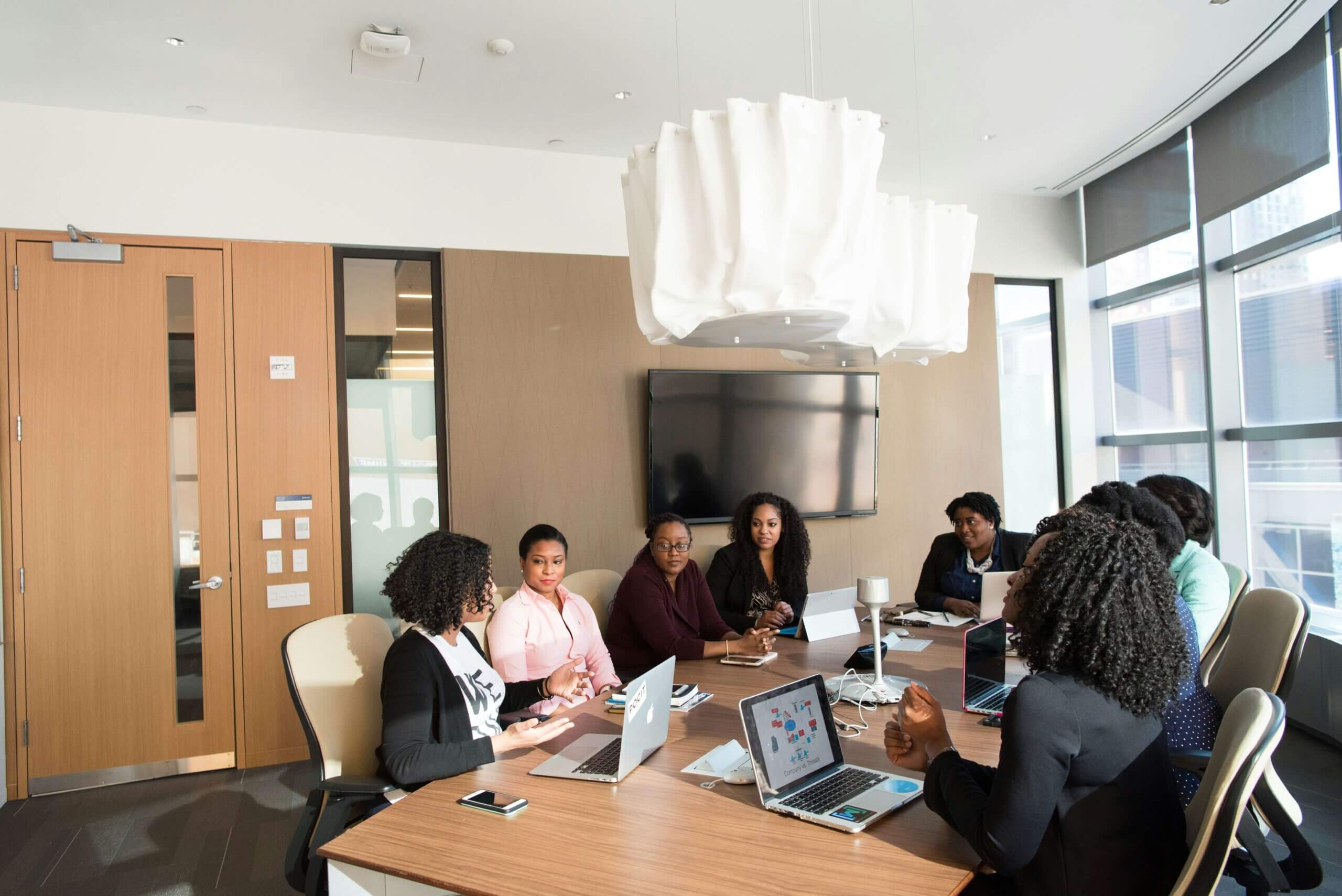 A diverse group of professionals engaged in a discussion around a modern conference table with laptops, emphasizing collaboration and inclusivity in workplaces for wellness.