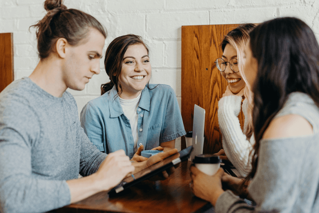 A group of remote work young professionals collaborating at a cafe, engaging in discussion with laptops and tablets.