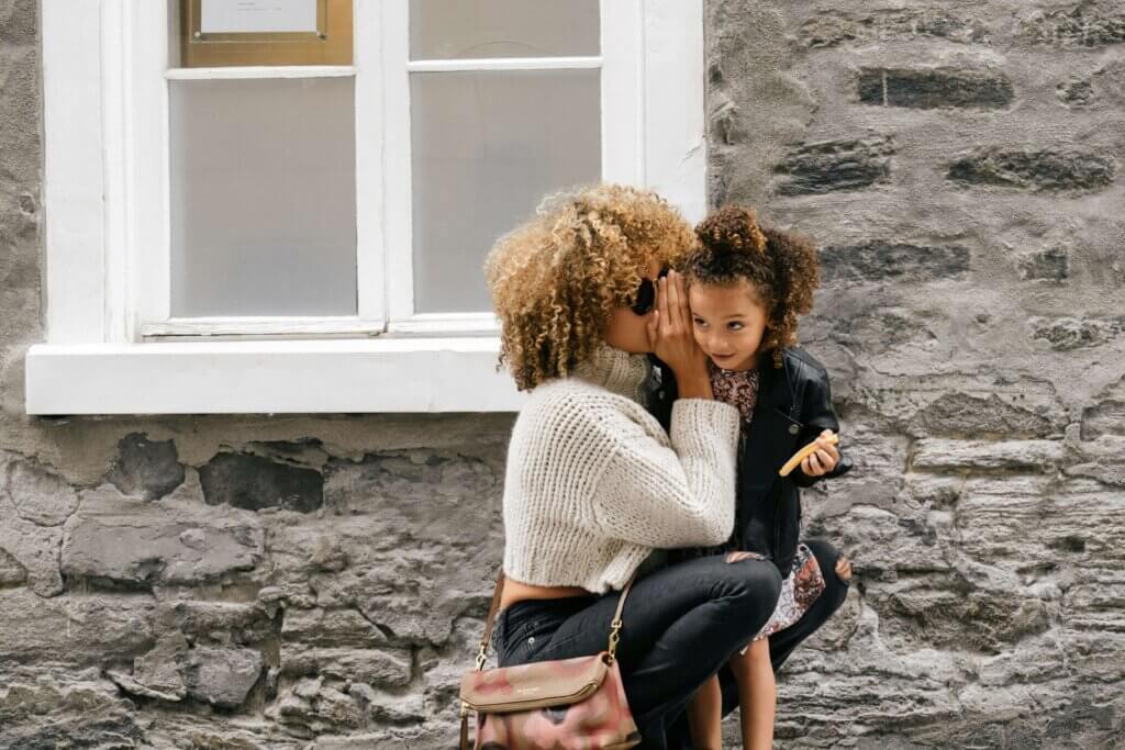 a woman is whispering something on her daughter's ear and smiling, which demonstrates balancing work and family life