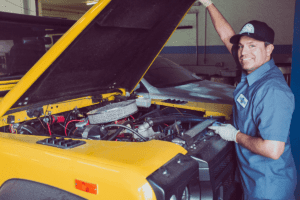 Smiling auto mechanic working on a yellow vehicle, symbolizing the idea to treat your professional development maintenance like your car maintenance plan.