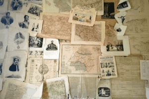 A collage of vintage maps, portraits, and newspapers pinned to a wall, offering resources for how to become a genealogist.