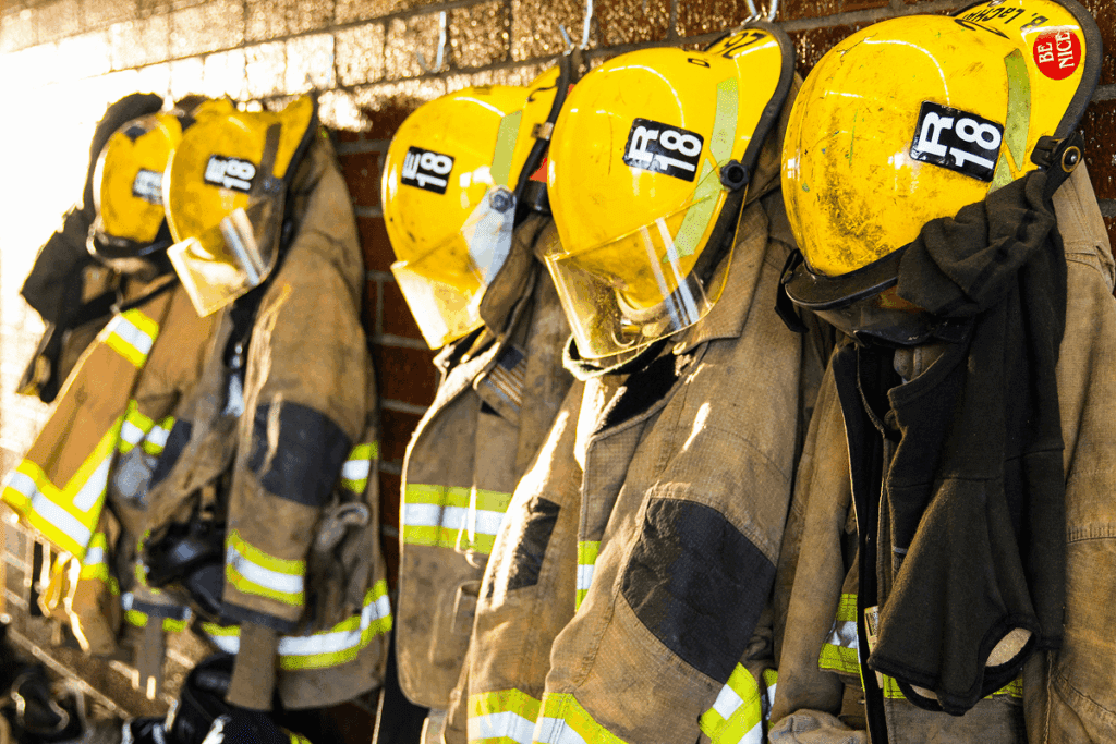Firefighting jackets and helmets hang on hooks in a station, ready for use, showing the organized setup of a fire station and how to become a volunteer firefighter by familiarizing oneself with essential gear.