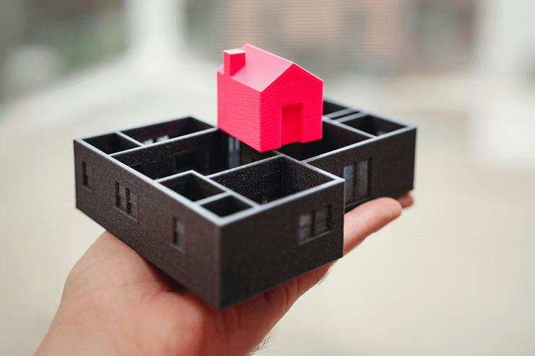 A hand holding a 3D printed model house on a black floor plan, symbolizing property management planning and design, perfect for learning how to become a property manager.