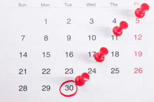 A calendar showing a month with red push pins on the 5th, 11th, 17th, 18th, and 24th, and the 30th circled in red, illustrating how many work days in a month might be highlighted for planning.