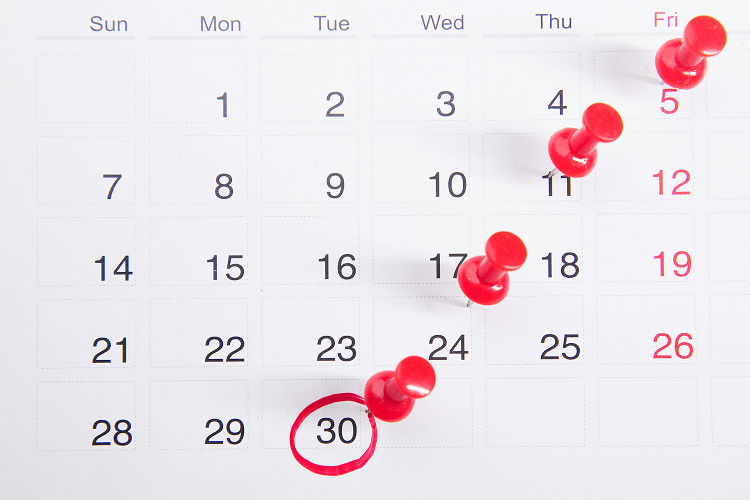 A calendar showing a month with red push pins on the 5th, 11th, 17th, 18th, and 24th, and the 30th circled in red, illustrating how many work days in a month might be highlighted for planning.