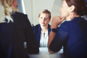 Image of a professional meeting with three individuals, one in focus wearing a blue blazer and white shirt, engaged in a job vs career discussion. The scene highlights a collaborative environment, ideal for career development insights.