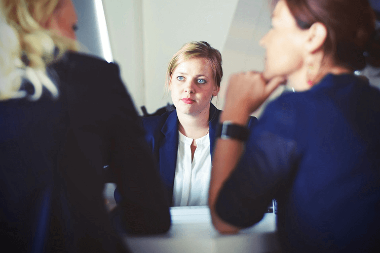 Image of a professional meeting with three individuals, one in focus wearing a blue blazer and white shirt, engaged in a job vs career discussion. The scene highlights a collaborative environment, ideal for career development insights.