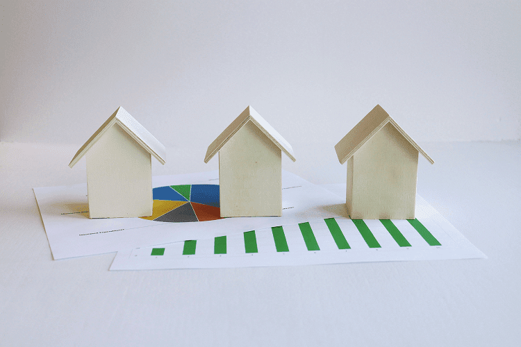 Three wooden model houses on top of financial charts with green bars and a pie chart, showcasing property market analysis, essential for anyone studying how to become a property manager.