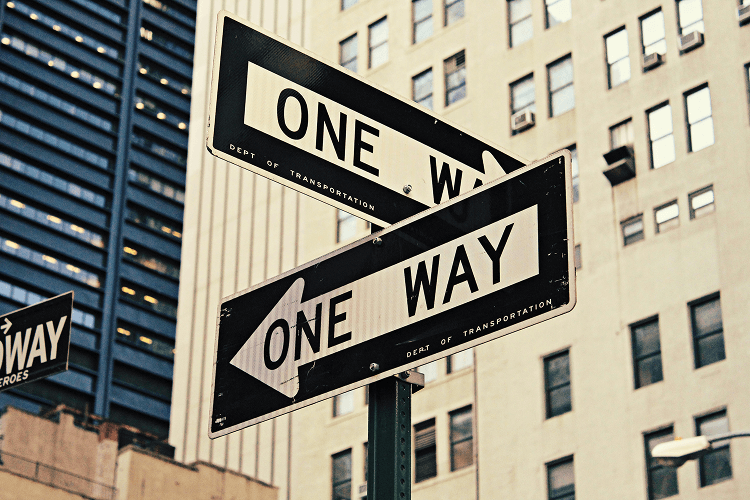 Image of two "One Way" street signs in an urban setting with tall buildings, symbolizing direction and decision-making in career development.