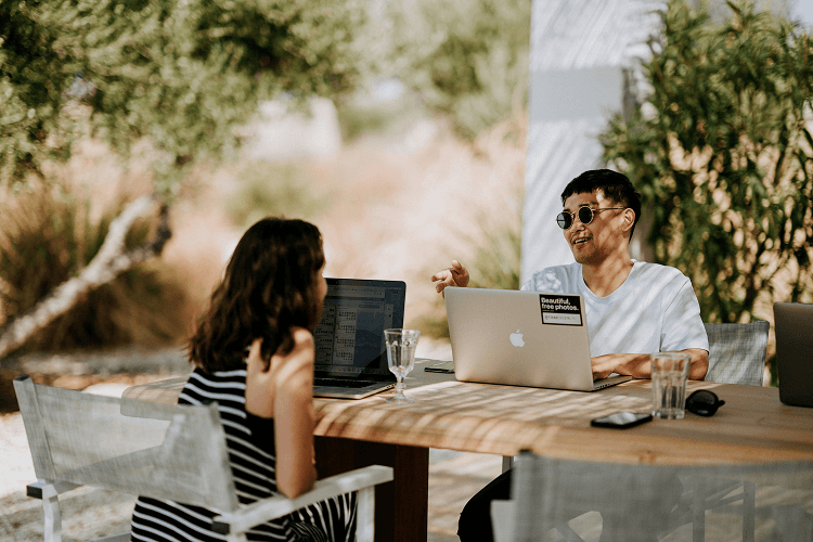 Two coworkers having an outdoor meeting with laptops, discussing projects and productivity, relevant to understanding how many work weeks in a year.