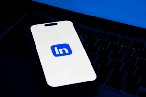 A smartphone with the LinkedIn app icon on its screen is placed on a laptop keyboard, highlighting how to get a job using LinkedIn.