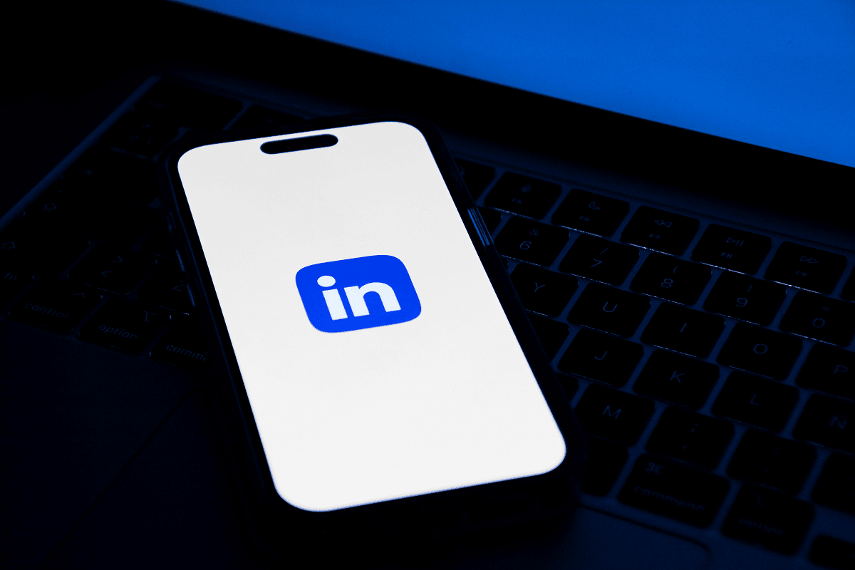 A smartphone with the LinkedIn app icon on its screen is placed on a laptop keyboard, highlighting how to get a job using LinkedIn.