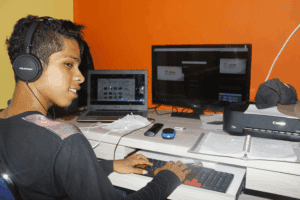 A teenage boy with headphones editing video on a dual-monitor setup, representing tech-savvy skills in a home office environment for what jobs hire at 13.